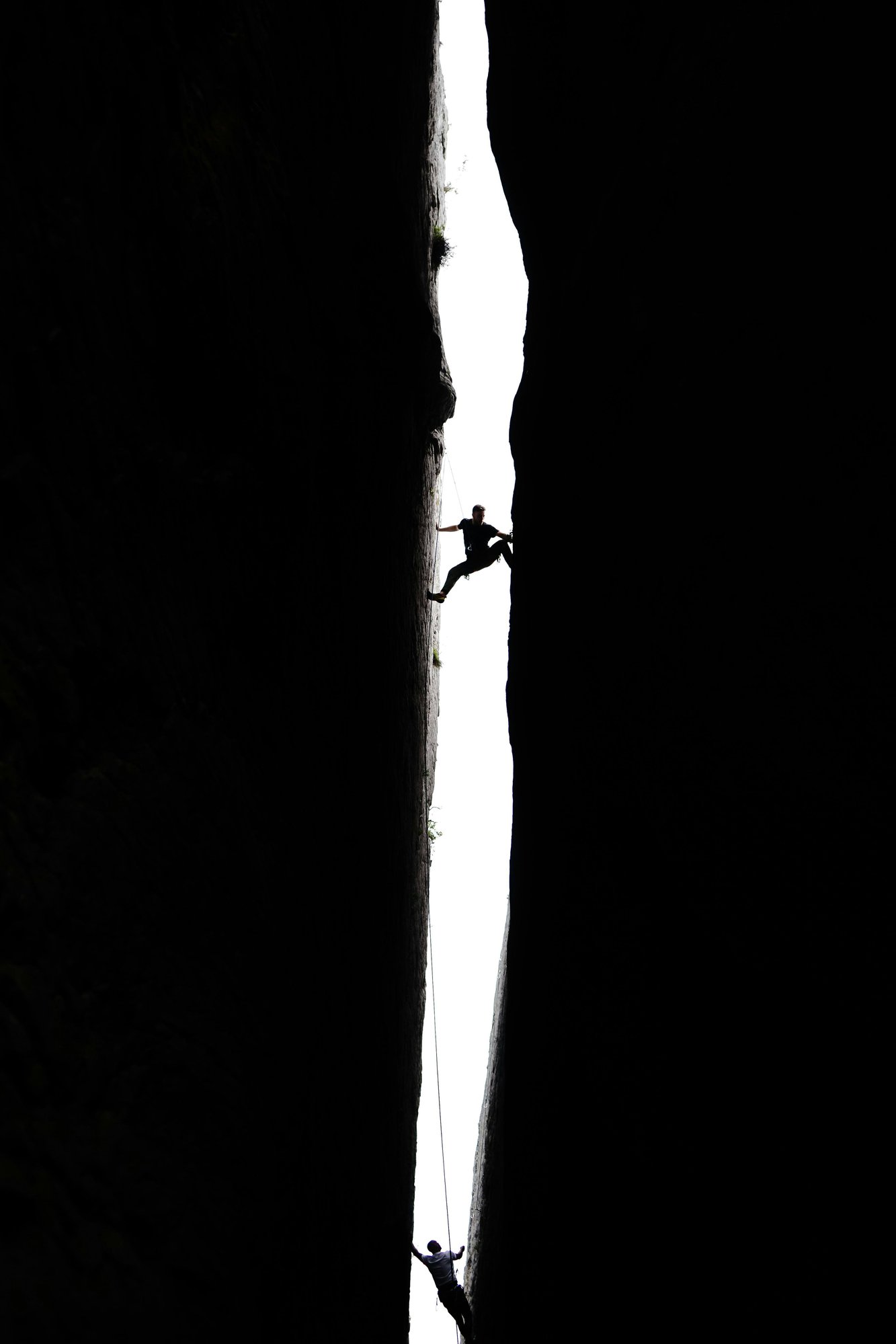 Two climbers scaling a steep rock crevice, representing challenge, resilience, and strategic growth.