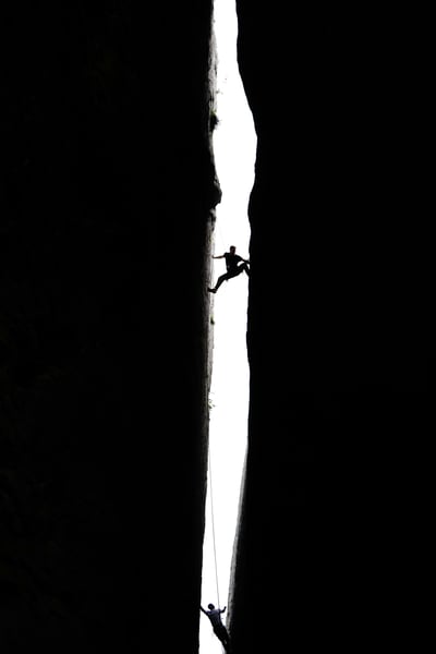 Two climbers scaling a steep rock crevice, representing challenge, resilience, and strategic growth.